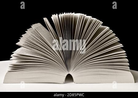 Paperback novel in monochrome, black and white photography. Open book isolated on black background. Stock Photo