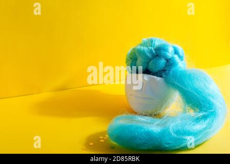 Decorative plaster handcraft pot in the shape of human face with blue artificial long hair on a yellow background with shadow, copy space. Stock Photo