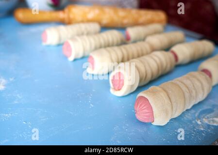 Blanks for fried pies. The sausages are wrapped in thin strips of yeast dough. The dough is rising. Selective focus Stock Photo