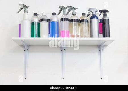 Shelf on a white wall in a workshop with a working tool - containers with sprayers and bottles with multi-colored liquids for cleaning, polishing and Stock Photo