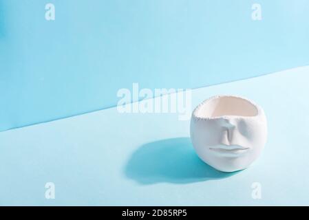 Decorative empty gypsum handcraft pot in the shape of human face on a duotone blue background with shadow, copy space. Stock Photo