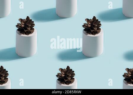 Abstract seamless pattern from solid three-dimensional gypsum figures cylinders with pine cone in the center on a pastel blue background, shadows and Stock Photo