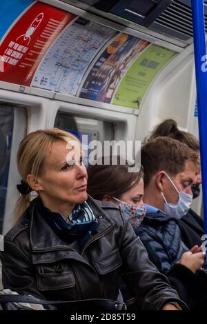 London, UK. 27th Oct, 2020. Most tube travellers wear mandatory masks but an increasing number are, once again, ignoring those rules or avoiding them with an exemption (despite the clear signage above the lady with the dog). Passenger numbers remain down, but are now rising. Just as the government begins to tighten its Coronavirus (covid 19) guidance again. Credit: Guy Bell/Alamy Live News