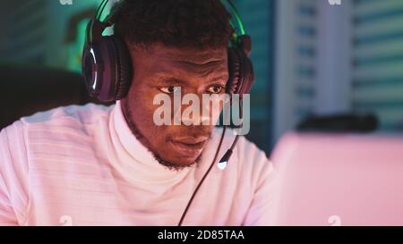 Happy young black man with illuminated headset using laptop. Home office and remote work concept. Stock trader portrait. High quality photo Stock Photo