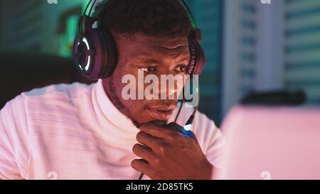 Happy young black man with illuminated headset using laptop. Home office and remote work concept. Stock trader portrait. High quality photo Stock Photo