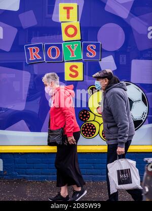 Senior couple wearing face masks walking past toy shop, Wroxham, Norfolk, England, UK