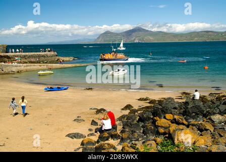 Couple sitting on roacks with Porth Dinllaen lifeboat and Yr Eifl Mountains in distance, Nefyn, Lleyn peninsula, Gwynedd,. North Wales. Stock Photo