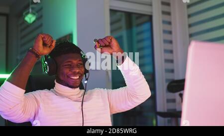 Happy young black man with illuminated headset using laptop. Home office and remote work concept. Stock trader portrait. High quality photo Stock Photo
