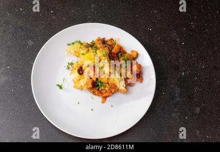 Lasagna served on a white plate at a dark kitchen table top Stock Photo