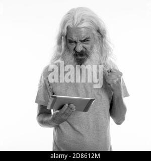 Studio shot of senior bearded man using digital tablet while looking angry Stock Photo