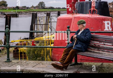 Senior man sitting on bench in harbour, Kings Lynn, Norfolk, UK Stock Photo