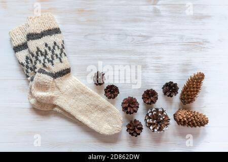 Warm wool socks for cold season and pine cones on vintage wood background. Woolen socks for winter on white wood surface with copy space for text Stock Photo