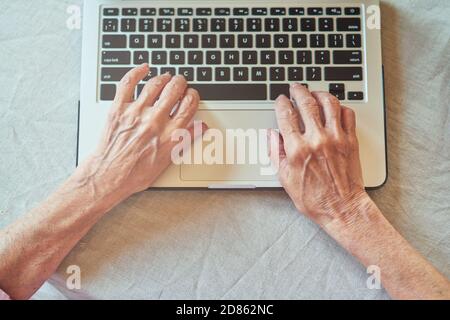 Top view of wrinkled female hands typing on laptop. Domestic lifestyle concept Stock Photo