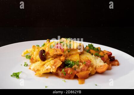 Lasagna served on a white plate at a dark kitchen table top Stock Photo