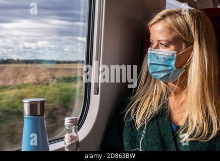 Woman wearing face mask on train looking through window Stock Photo