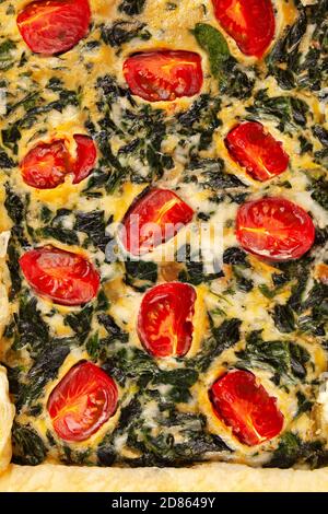 Detail of spinach pie or quiche with cheese and tomatoes from above. Stock Photo