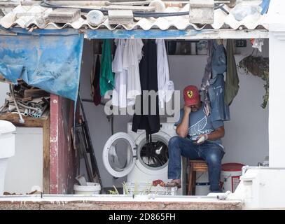 Man sitting next to washing machine looking at his mobile phone. Stock Photo