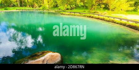 Hot pool in a tropical forest, bright and beautiful emerald hot pool with wooden fence at dusk. Focus on the stone on the hot pool. Thailand. Stock Photo