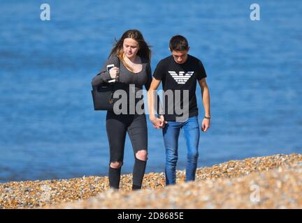 Young couple holding hands walking on a beach at the seaside, with sea (ocean) behind them in England, UK. Stock Photo