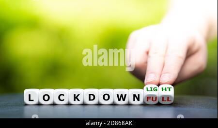 Symbol for a second lockdown. Hand turns dice and changes the expression "lockdown full" to "lockdown light". Stock Photo