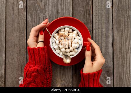 Womans hands holding hot chocolate with marshmallow in red cup Stock Photo