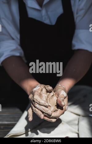 Close up of woman hands works with clay. Female potter kneads and moistens the clay before work. Stock Photo