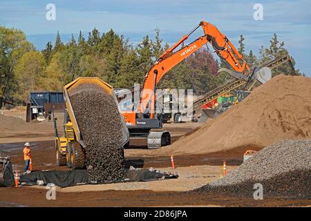 A large, earth moving dump truck on a construction site in Bend, Oregon, moves gravel from a rock crusher to foundation pit. The construction site is Stock Photo