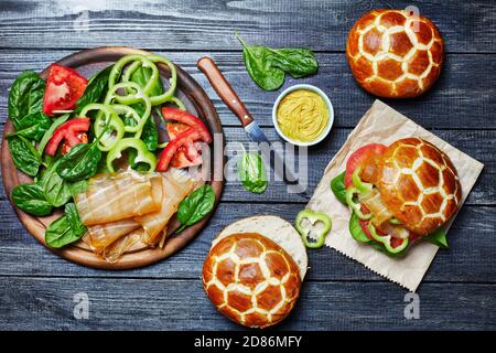 Fish burgers of chinese pineapple buns with spinach, sweet pepper, dried tuna, and tomatoes served on a round cutting board with mustard on a dark woo Stock Photo
