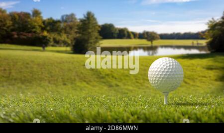 Golf sport and leisure in nature, golf club course. Golfball on green lawn grass, landscape with trees and a small pond, blue sky background. 3d illus Stock Photo