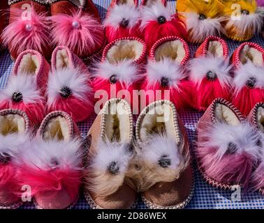Handmade souvenirs of the mountain Crimea for tourists. Warm cozy funny multi-colored fur Slippers with a fluffy pom pom. Stock Photo