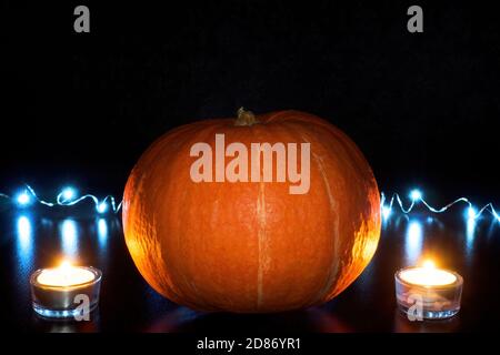 Orange pumpkin and two burned tea candles on black background with blue garland. Halloween concept Stock Photo