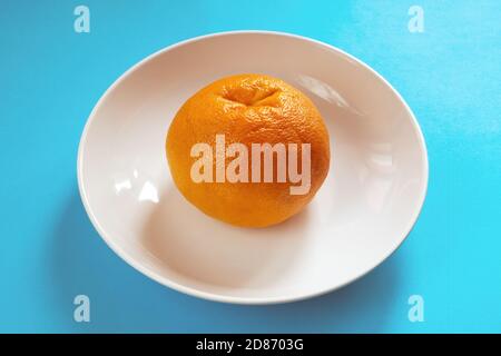 Whole orange grapefruit on white plate on blue background. Diet concept Stock Photo