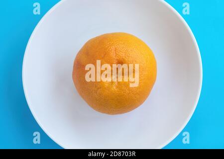 Top view of one orange grapefruit on white plate on blue background. Diet concept Stock Photo