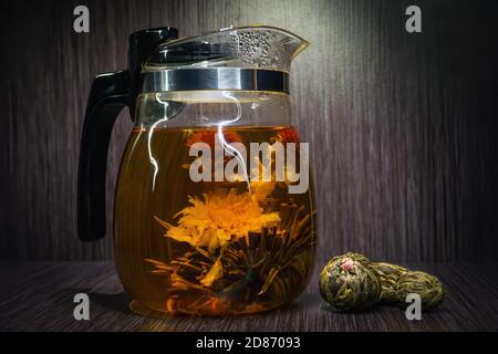 Blooming tea flower in glass teapot and dry flowering tea balls. Stock Photo