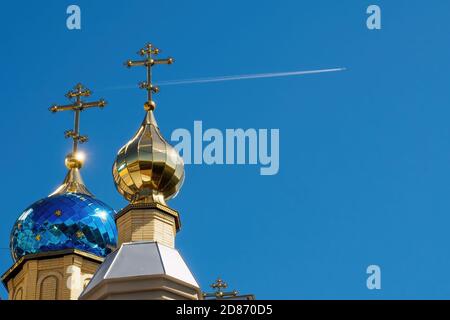 Domes of the temple with crosses against blue sky and flying plane with white trace. Orthodox church and flying airplane Stock Photo