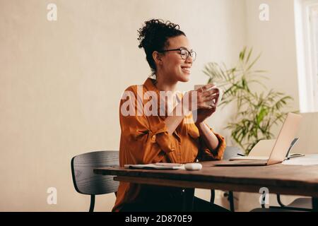 Woman having coffee and looking at laptop. Female taking a coffee break while working from home. Stock Photo