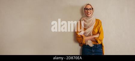 Portrait of a happy muslim woman standing against a wall. Female entrepreneur looking at camera and smiling. Stock Photo