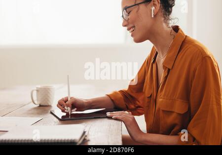 Woman wearing wireless earphones using digital tablet. businesswoman working from home, making notes on her digital tablet with stylus. Stock Photo