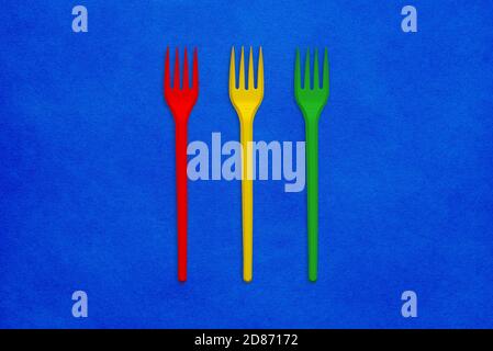 Red, yellow and green plastic fork on a blue background. Colorful minimal style Stock Photo
