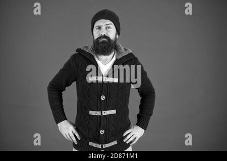 Winter season menswear. Personal stylist. Warm and comfortable. Fashion menswear shop. Masculine clothes concept. Winter menswear. Clothes design. Man bearded warm jumper and hat red background. Stock Photo