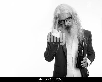 Studio shot of senior bearded businessman holding bottle of beer and looking tired Stock Photo