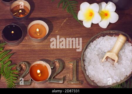 Top view of spa composition with white sea salt plumeria flowers and numbers 2021 illuminated by burning candles. Stock Photo