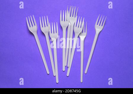 White plastic forks on a purple background. Disposable tableware for a picnic, lunch or dinner. A top view of a flat layout Stock Photo