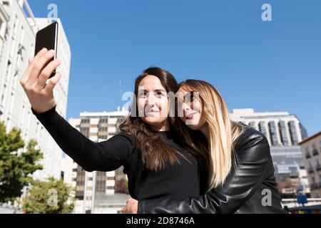 Two girls hugging and taking a selfie in the city. Stock Photo