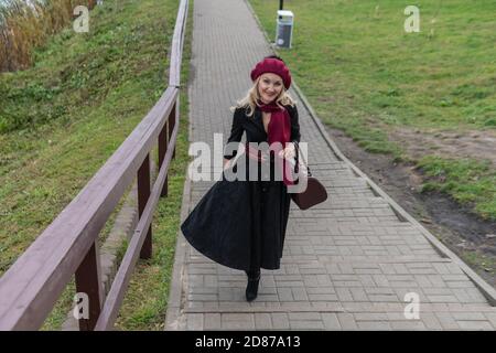 A beautiful woman walks up the stairs and in burgundy pall and biret, an adult with a beautiful smile in black clothes, in the fall against the Stock Photo