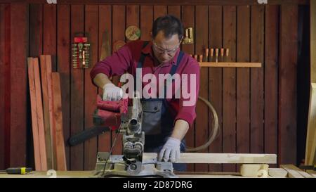 Man carpenter cuts a wooden beam with a circular saw in the workshop. Stock Photo