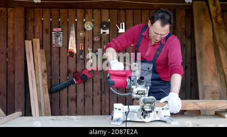 Male joiner processes wood bar using a miter saw in a workshop. Stock Photo