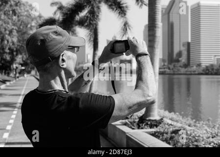 Senior tourist man wearing cap while taking pictures at peaceful park in Bangkok Thailand Stock Photo
