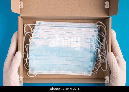 Top overhead above close up view photo of doctor hands holding unpacking unwrapping cardboard box full of facial medical masks inside isolated over bl Stock Photo