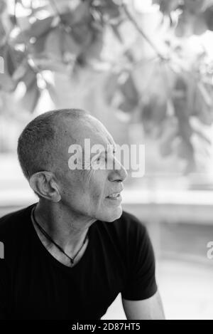Profile view of bald senior tourist man thinking and relaxing under the tree in the city Stock Photo